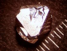 A single crystal of YFe2Zn20 is shown next to a mm scale.  It grows in this shape naturally and has mirrored facets.
