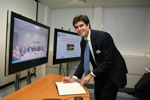 ORNL Director Thom Mason signs the memorandum of understanding during a visit to the Imperial College of London for the launch of the Global Lab. In the background are Oak Ridge officials looking on via teleconference from ORNL.