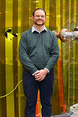 College of William and Mary Graduate Student Matthew Burton with a cavity deposition system at Jefferson Lab that Burton is using in his research to improve superconducting radiofrequency thin-film capabilities.