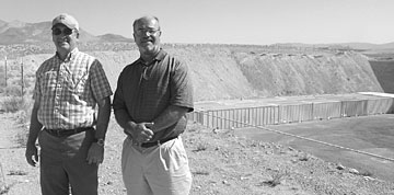 Jim Terry (left) and Bill Hermes pay their respects at the Nevada Test Site, the final resting place of 21,000 barrels of surplus thorium nitrate, shown in the background.